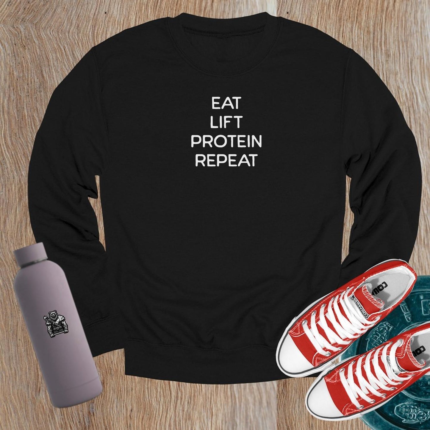 "Black crewneck sweatshirt featuring bold white text 'Eat, Lift, Protein, Repeat'. Ideal for gym workouts and casual wear, inspiring fitness."