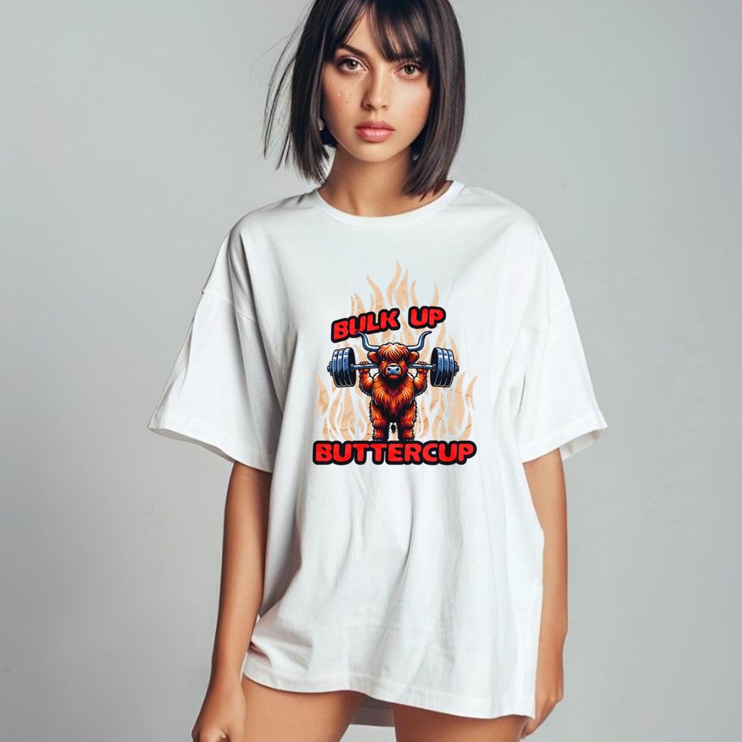 Alt text: "Bulk Up Buttercup T-shirt featuring a fierce weightlifting Highland cow surrounded by vibrant flames, perfect for gym enthusiasts."
