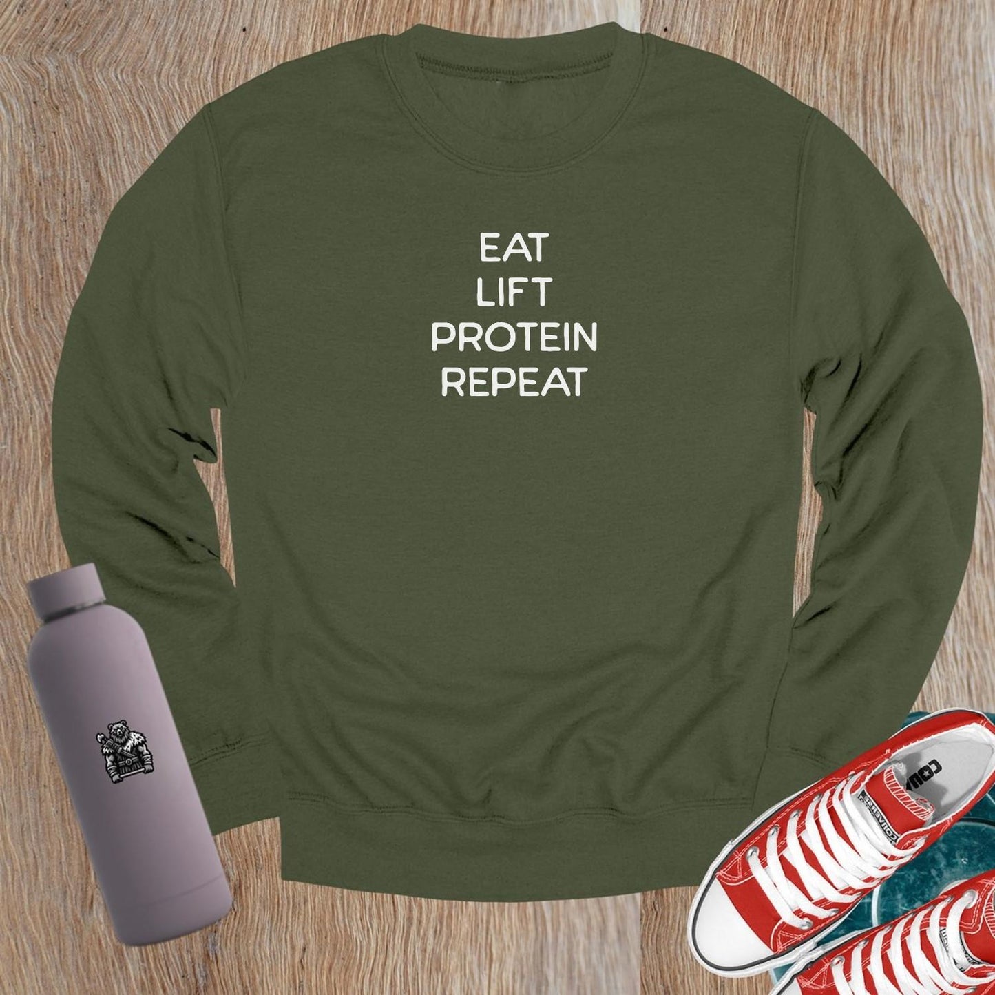 "Black crewneck sweatshirt featuring bold white text 'Eat, Lift, Protein, Repeat'. Ideal for gym workouts and casual wear, inspiring fitness."